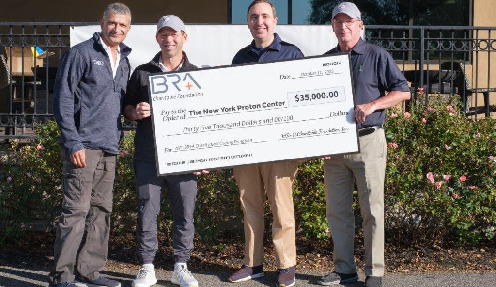 Two men presenting giant check to New York Proton Center at golf tournament