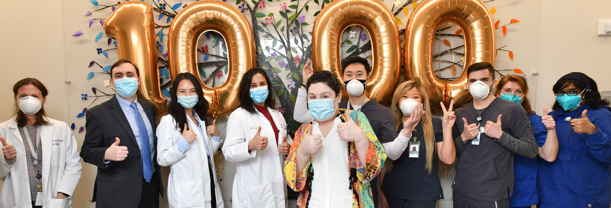 Staff at NYPC stand with their 1000th patient in front of large gold numerical balloons displaying "1000".